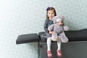 girl with toy teddy bear sitting on clinic table