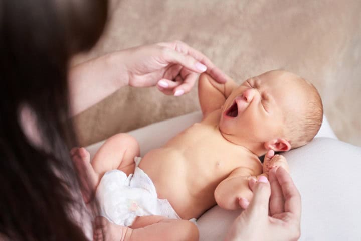 Yawning newborn baby lying down while mother gently holds the infant's arms