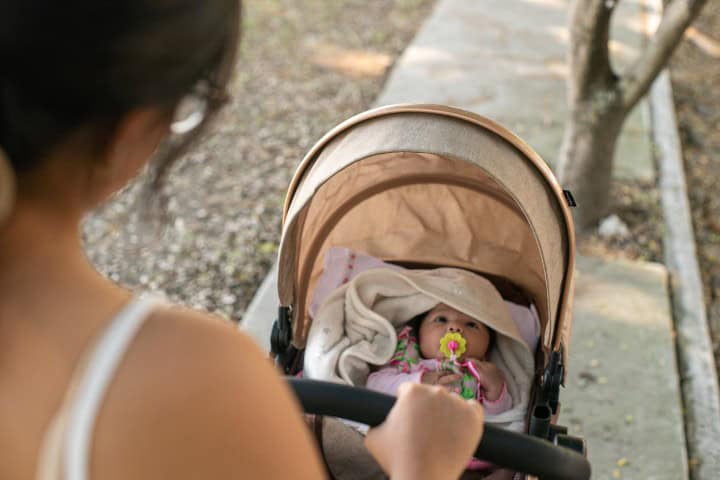 Baby in a stroller outdoors, covered with a blanket and holding a pacifier