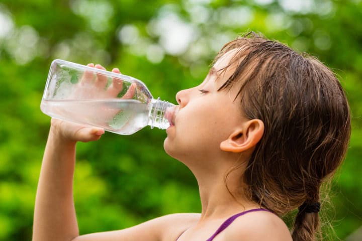 Young girl with wet hair, wearing a purple swimsuit, drinking water from a clear bottle