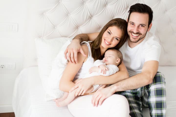 Loving family with mother and father smiling while holding their peacefully sleeping infant