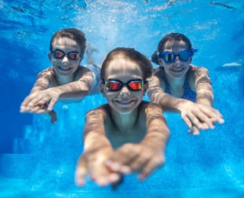 three happy kids swimming underwater in pool