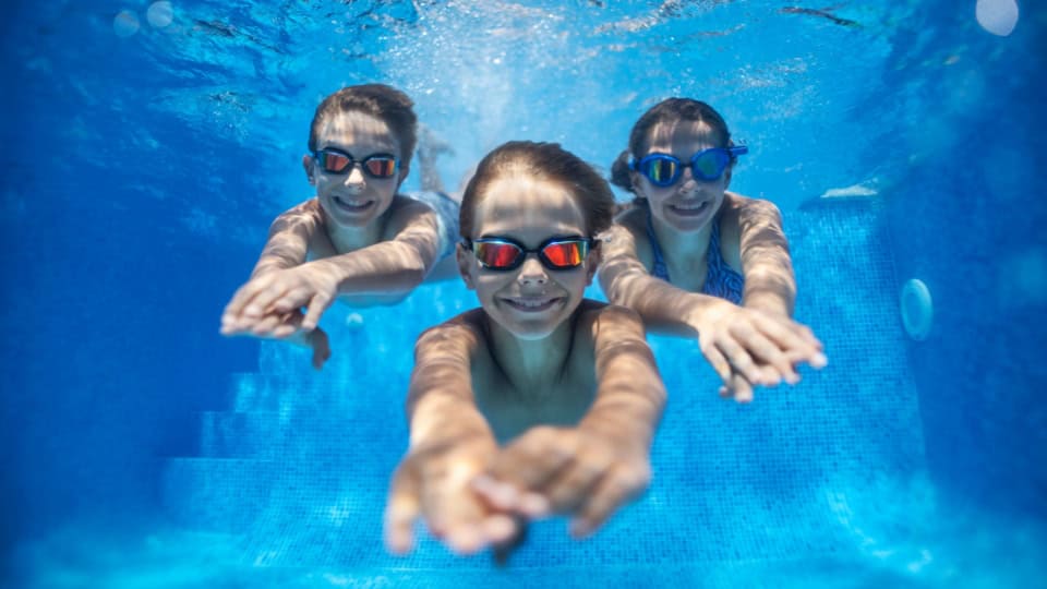 three happy kids swimming underwater in pool