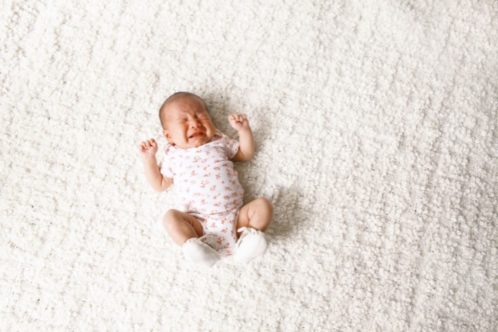 Crying newborn baby lying on a white, soft surface, expressing discomfort