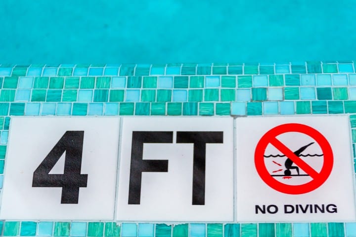 Safety sign at the edge of a swimming pool displaying '4 FT' to indicate the water depth, accompanied by a 'NO DIVING' symbol with a prohibition sign over a diver illustration