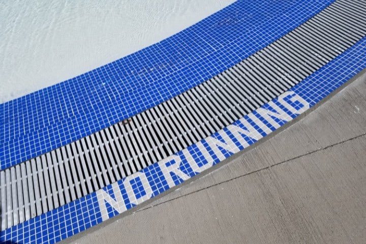 Curved blue and white tiled pool edge with the safety message 'NO RUNNING' spelled out in white letters on blue tiles