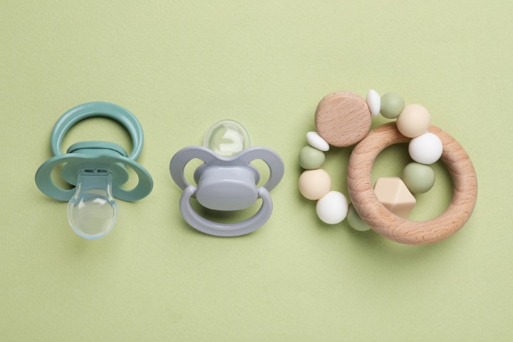 Two pacifiers and a wooden teething ring with silicone beads on a green background