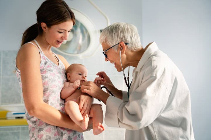 Pediatrician using a stethoscope to examine a newborn baby held by the mother