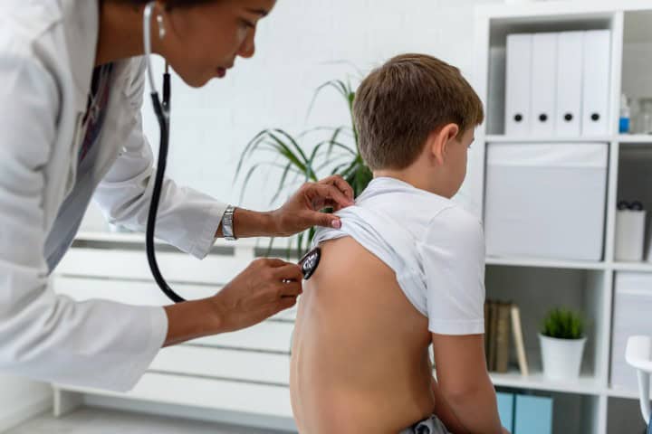 Pediatrician using a stethoscope to check the respiratory health of a young boy in a clinic