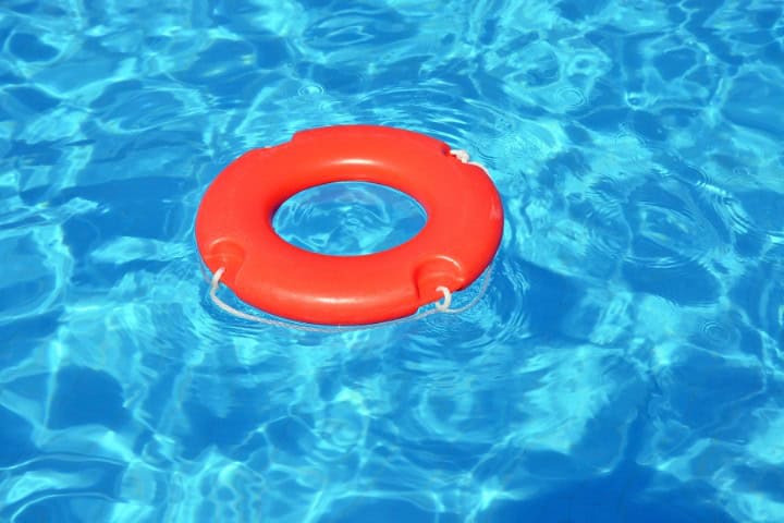 Bright orange lifebuoy floating in clear blue swimming pool water, with light ripples around it