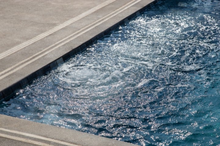 Turbulent water at the edge of a swimming pool, with sunlight reflecting off the dynamic ripples and splashes