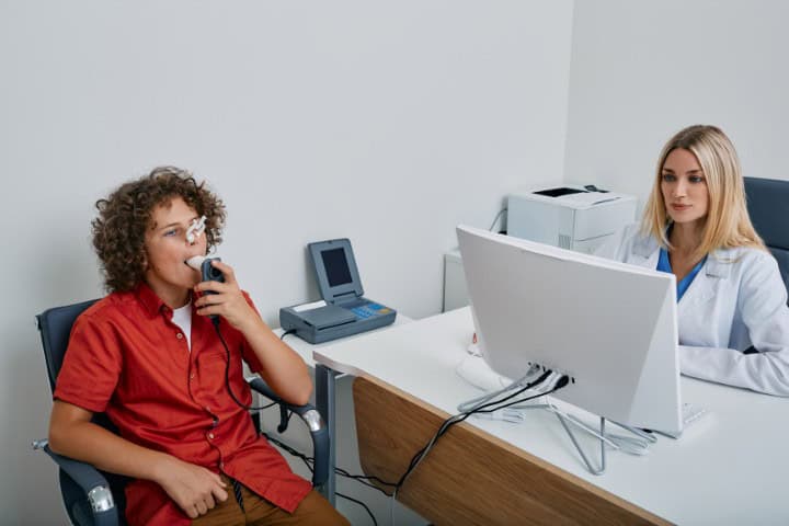 Young male patient using respiratory testing equipment while a pediatrician reviews the data in a medical office