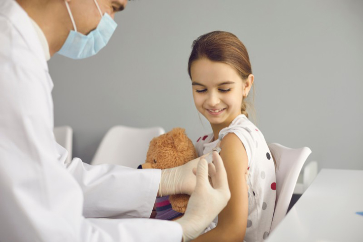 A pediatrician giving a vaccination to a cheerful girl holding her stuffed toy at a clinic