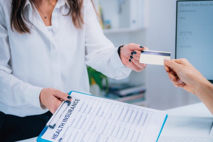 Close-up of a receptionist receiving an insurance card and providing a health insurance document to a patient