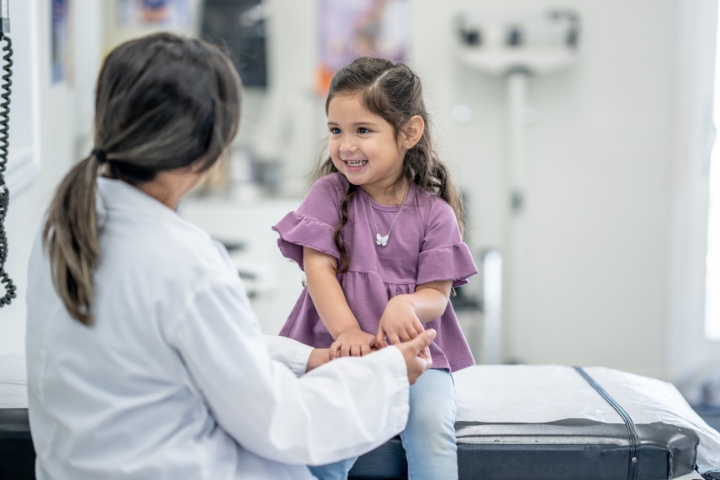 A pediatrician holding hands with a smiling young girl during a check-up in a medical examination room