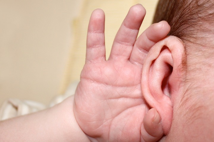 Close-up of baby’s hand near ear, symbolizing hearing awareness