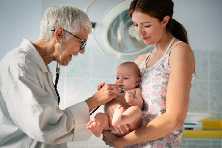 Mother holding baby as pediatrician conducts a health examination