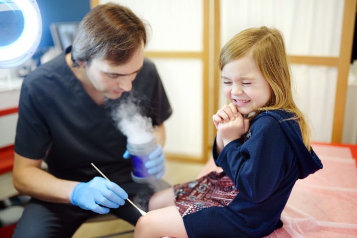 Pediatrician performing cryotherapy on a young girl's knee in a clinic