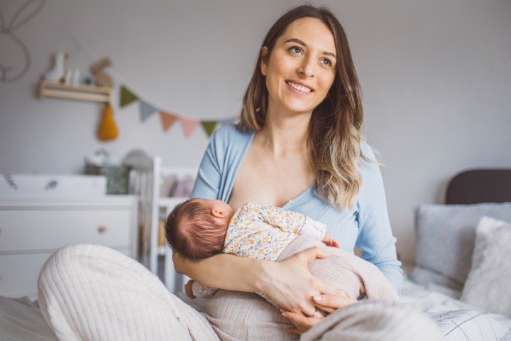 A smiling mother breastfeeding her newborn baby in a cozy nursery