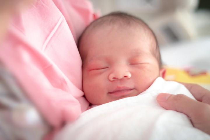 Newborn baby wrapped in a blanket, looking content post-frenotomy treatment.