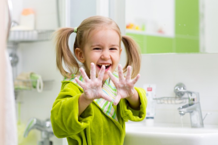 Smiling young girl washing her hands with soap in a bathroom