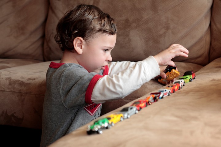 Child arranging toy cars in a repetitive pattern, indicating possible developmental challenges