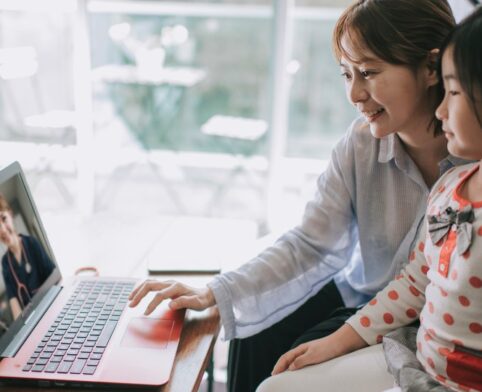 Mother and child engaging in a pediatric telehealth consultation on a laptop with a doctor visible on the screen