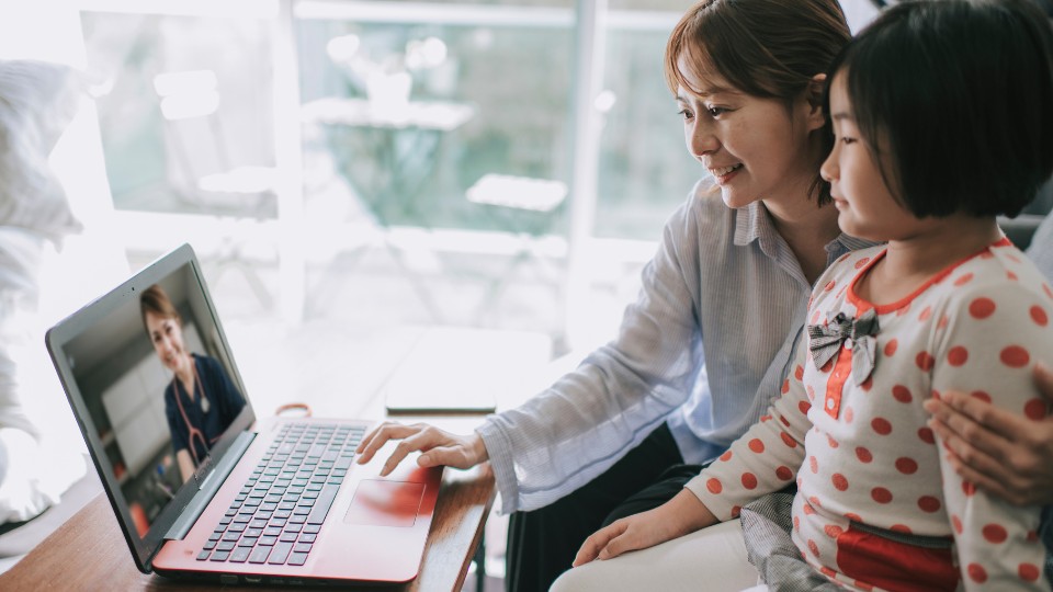 Mother and child engaging in a pediatric telehealth consultation on a laptop with a doctor visible on the screen