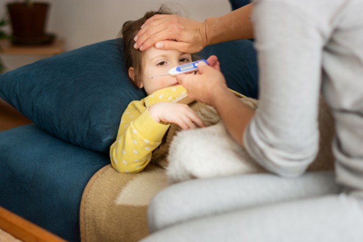 A parent checking a sick child's temperature, contemplating telemedicine or in-person visit