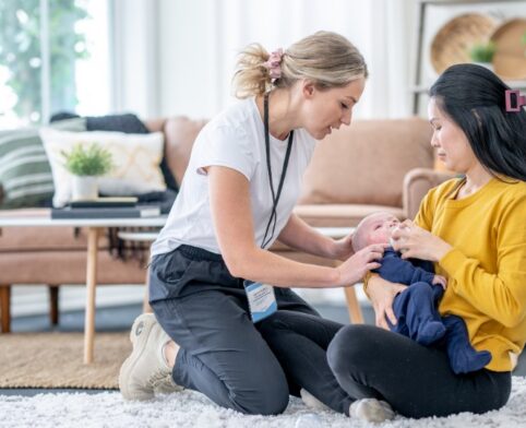 Lactation consultant providing hands-on breastfeeding guidance to a mother and her baby