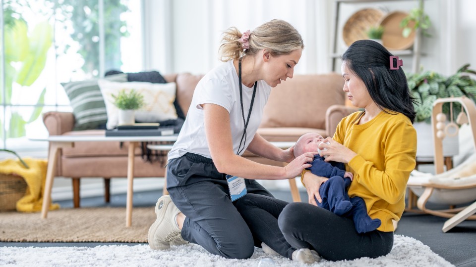 Lactation consultant providing hands-on breastfeeding guidance to a mother and her baby