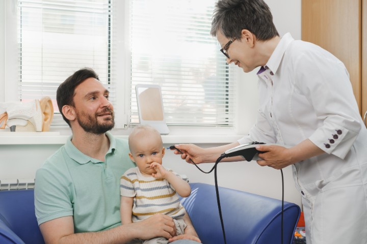 An audiologist conducting a hearing screening for a baby with a concerned parent