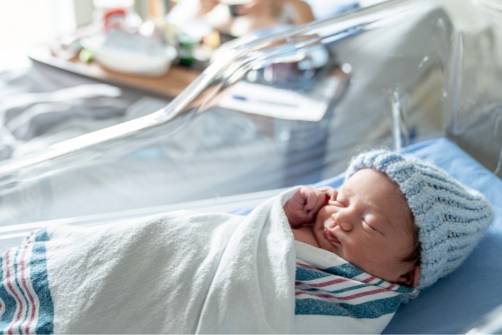 A newborn wrapped in a blanket resting in a hospital crib