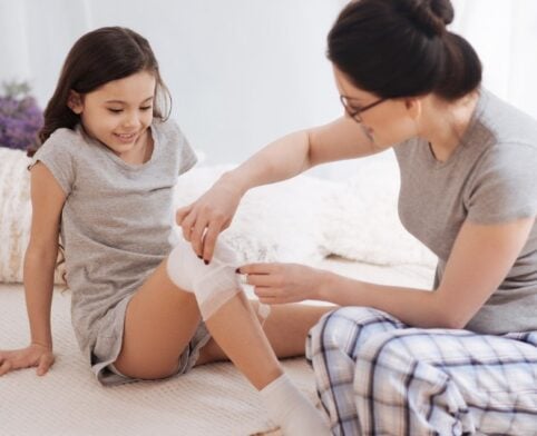 Mother applying a fresh bandage to a child's knee after cryotherapy treatment