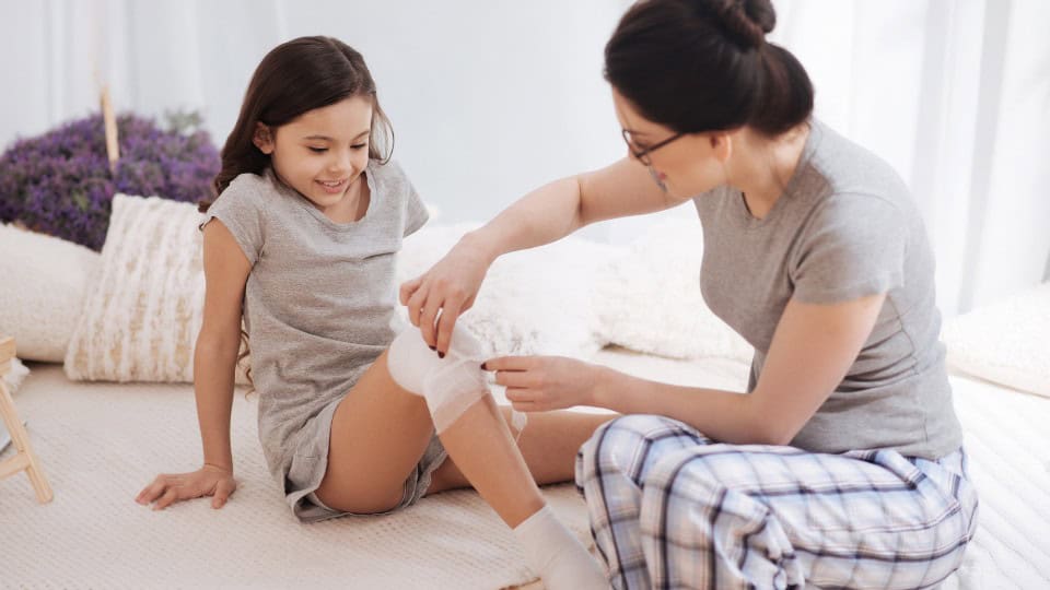 Mother applying a fresh bandage to a child's knee after cryotherapy treatment