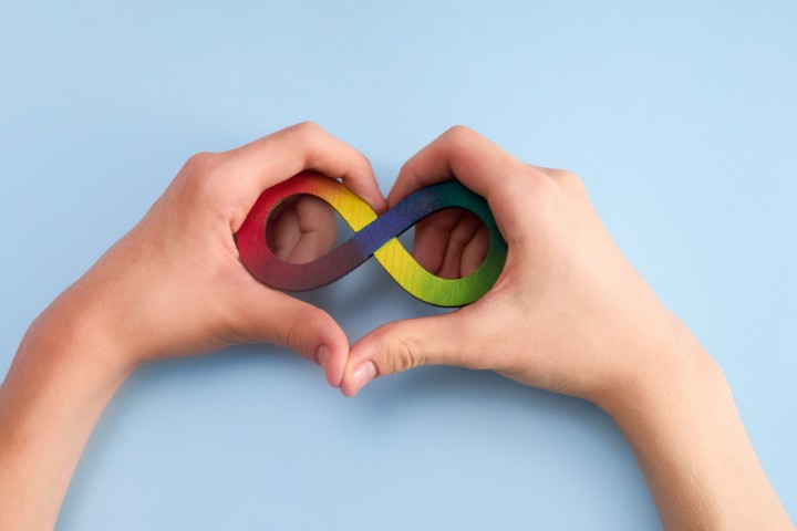 Hands forming a heart shape around a rainbow infinity symbol for autism awareness