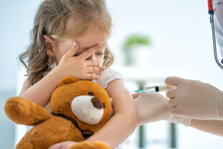 Nervous child receiving flu shot while clutching teddy bear
