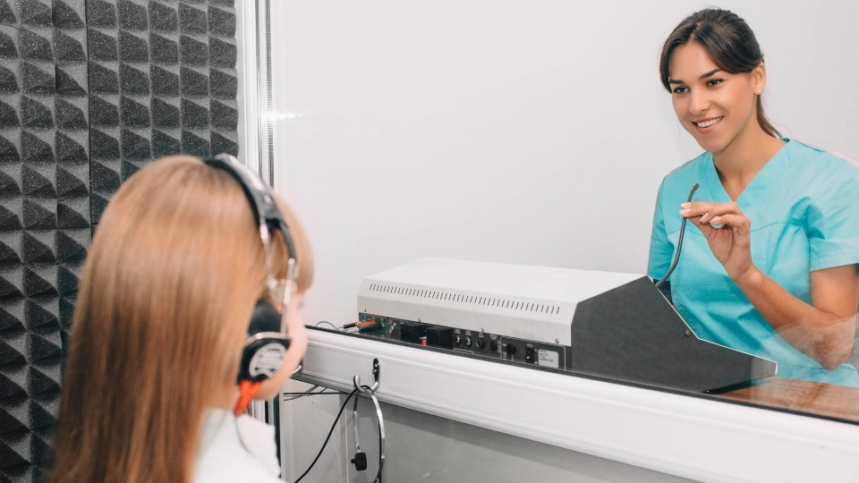 A family audiologist conducting a hearing screening for a child in a soundproof booth