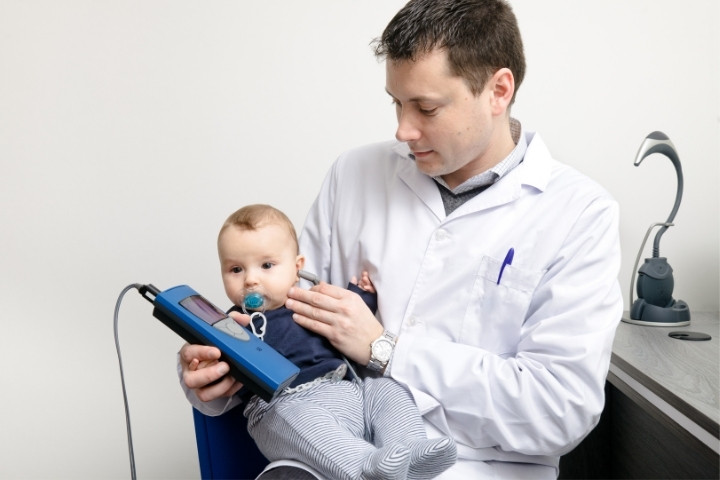 Audiologist holding an infant during a hearing test using diagnostic equipment