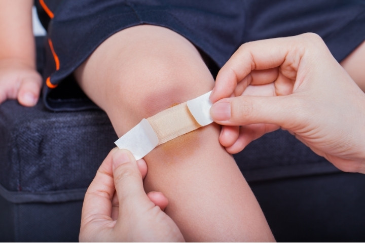 Parent covering a child’s knee with a bandage to help prevent picking and reduce wart spread.