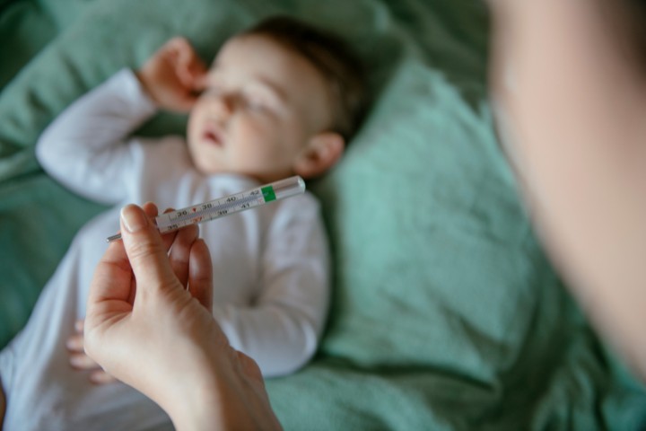 Thermometer held near a baby resting in bed during fever monitoring