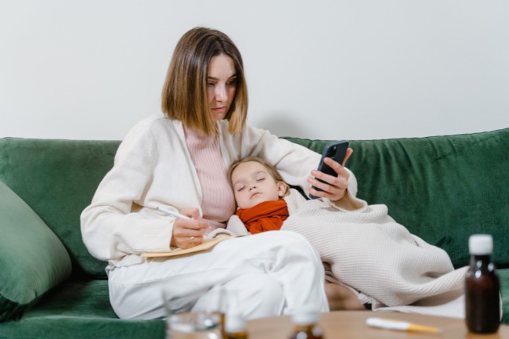 Mother monitoring child symptoms while checking visit summary after a pediatric telehealth visit