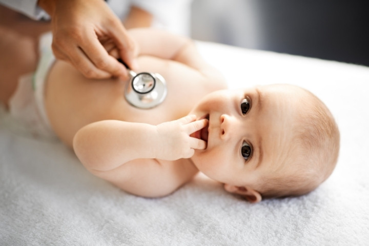 Baby lying on an exam table while a pediatrician performs a preventive care checkup
