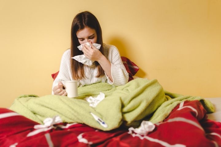 Teen resting in bed with tissues while experiencing flu symptoms