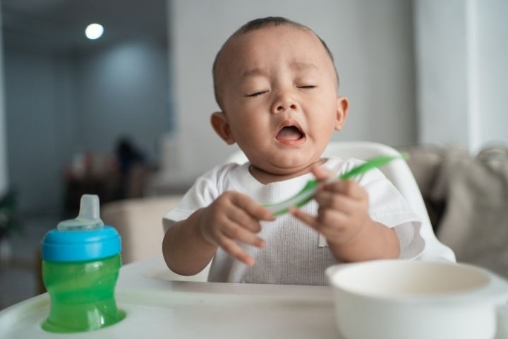 Infant appearing fussy and sneezy while sitting in a high chair