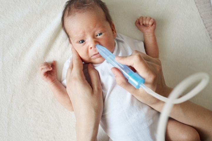 Newborn with flu receiving help clearing nasal congestion from the nose