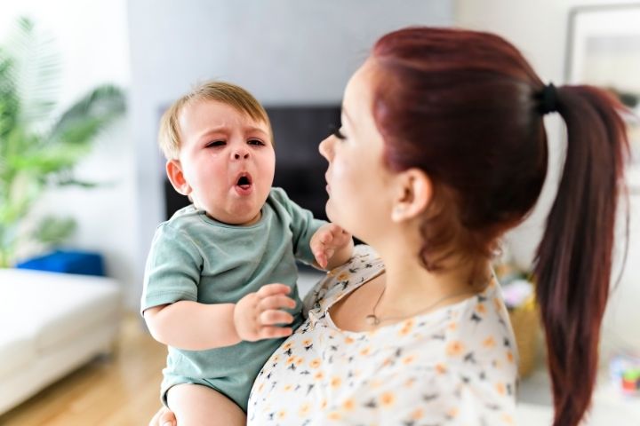 Mother holding a coughing baby, which can be a possible symptom of childhood asthma