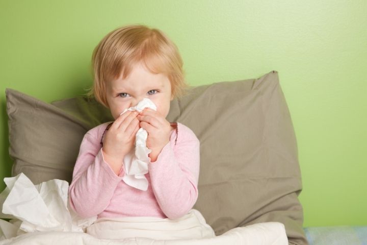 Preschool-age child exhibiting flu signs using a tissue for a runny nose